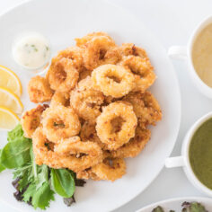 Kızarmış kalamar dilimleri, tabakta düzenli bir şekilde yerleştirilmiş, yanında limon dilimleri ve yeşilliklerle süslenmiş.